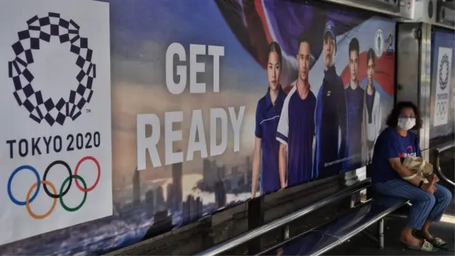 Woman wearing a mask at a bus stop with Tokyo 2020 advertising