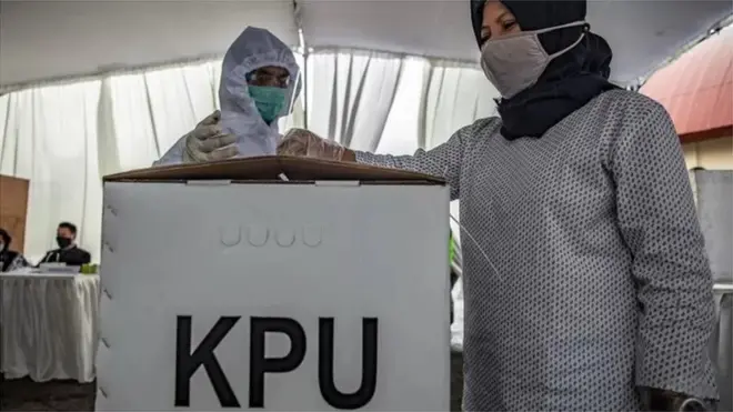 Petugas Kelompok Penyelenggara Pemungutan Suara (KPPS) berpakaian hazmat mendampingi warga memasukkan surat suara ke dalam kotak saat Simulasi Pemungutan dan Penghitungan Suara Pemilihan Bupati dan Wakil Bupati Semarang 2020 di Bergas, Kabupaten Semarang, Jawa Tengah, Minggu (29/11).
