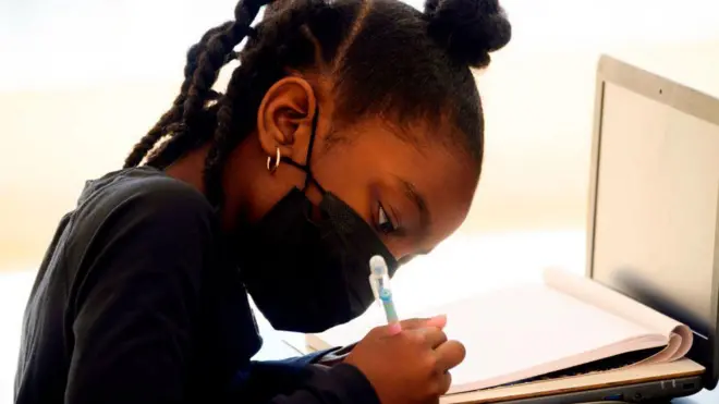 Menina de máscara estudando em frente a laptop
