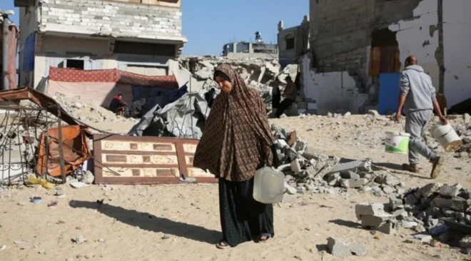 팔레스타인 이주민 여성인 마크람 함두나가 2024년 12월 19일 가자지구 남부에 위치한 대피소 밖에서 물통을 들고 있다