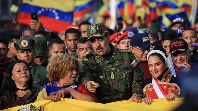 Moduro ortada, etrafında kadınlar, arkasında kalabalık ve Venezuela bayrakları var.