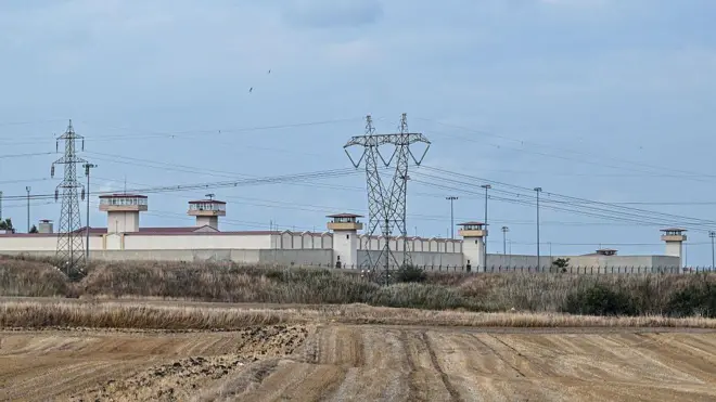 Silivri Cezaevi'nin duvarlarının önünde yüksek gerilim hatları ve bir tarla görülüyor