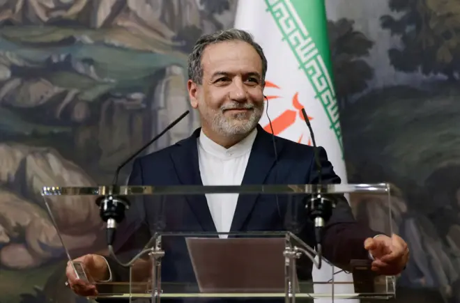 Министр иностранных дел Ирана Аббас Аракчи на фоне флага Ирана (18 апреля 2025 года)