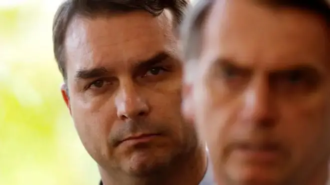 Jair Bolsonaro em imagem desfocada, com seu filho, Flávio, aparecendo atrás 