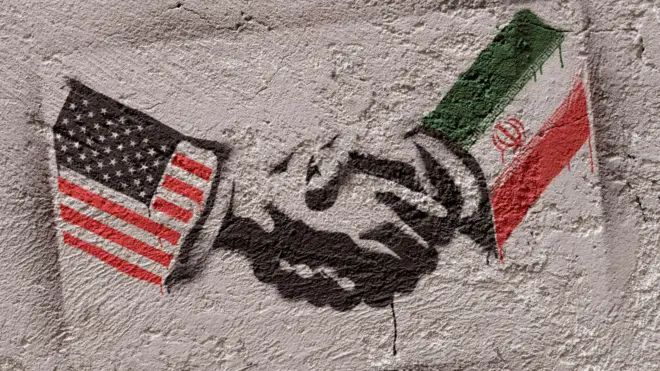 عکسی از یک گرافیتی در تهران. دستهای دو نفر دیده میشوند که با هم در حال دست دادن هستند. آستین یکی از دستها پرچم ایران و آستین دیگری، پرچم آمریکاست.