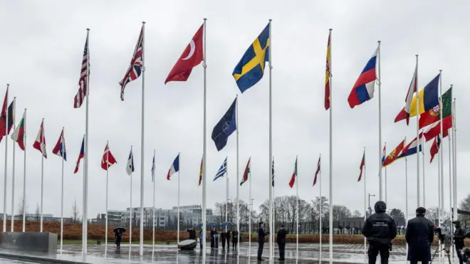 NATO Karargâhı avlusunun fotoğrafı. Ortada bir NATO bayrağı, etrafında ise müttefiklerin bayrakları dikili. 