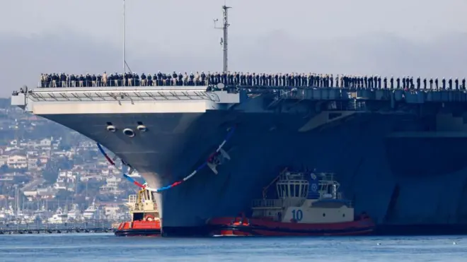 حاملة الطائرات الأمريكية "يو أس أس أبراهام لينكولن"، تظهر ضخمة وتقف في وسط مياه البحر، وعلى متنها أفراد تابعون للبحرية الأمريكية والجيش الأمريكي.