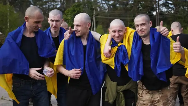 خمسة أوكرانيين مفرج عنهم يقفون مبتسمين وعلى أكتفاهم علم أوكرانيا بعد وقت قصير من إطلاق روسيا سراحهم