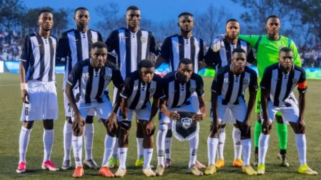 Abakinnyi b'ikipe ya APR FC yo mu Rwanda bahagaze mu kibuga barimo kureba muri 'camera'. Bambaye imyenda y'umweru n'umukara, mu gihe umunyezamu wayo yambaye imyenda y'umuhondo. 
