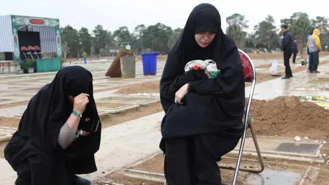 Two women crouch at the grave of a relative in a cemetary in Tehran on 16 March