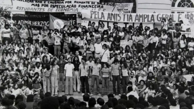 Dezenas de manifestantes em foto em preto e branco; ao fundo, lê-se cartaz que diz: 'Pela anistia ampla, geral e irrestrita'