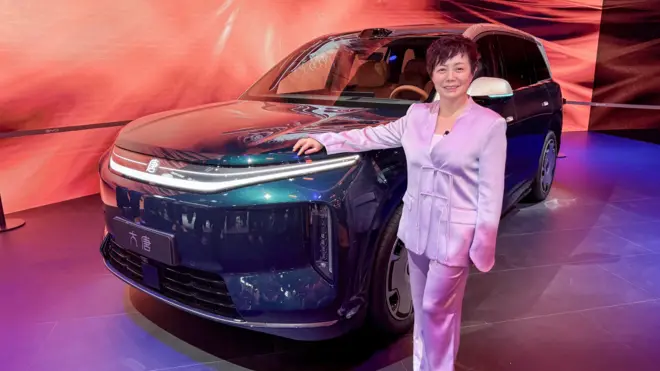 Bà Stella Li diện một bộ vest lụa màu hoa tử đinh hương, tựa người vào chiếc SUV của BYD khi đang trả lời phỏng vấn BBC tại Triển lãm Ô tô Bắc Kinh