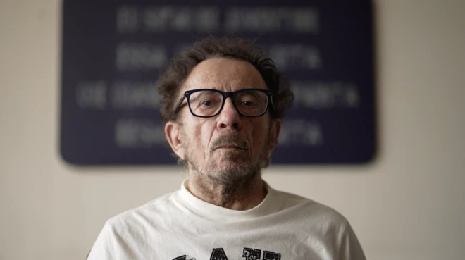 Tom Zé encara a câmera, com quadro escuro ao fundo