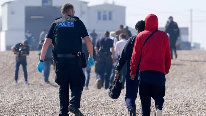 One police officer escort one group of pipo dem reason to be migrants ashore from di Dungeness lifeboat for Dungeness, Kent