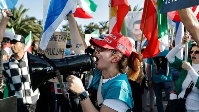 شماری از تظاهرکنندگان با پرچمها، زنی بلندگویی در دست دارد