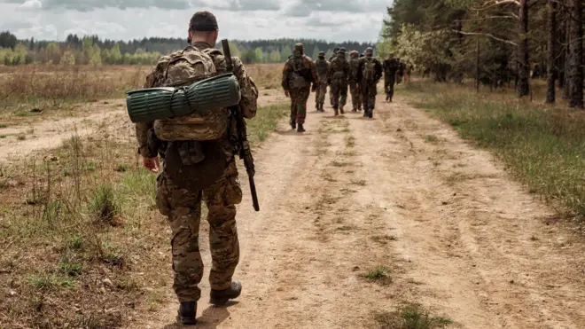 Военный в полном обмундировании идет по проселочной дороге