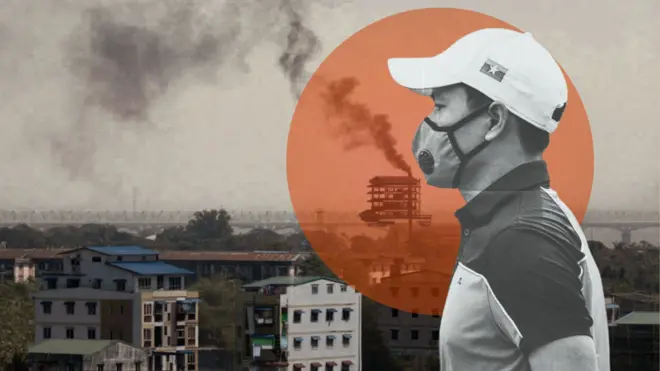 ရန်ကုန်မြို့က စက်ရုံတစ်ခုရဲ့ မီးခိုးခေါင်းတိုင်ကနေ မီးခိုးလုံးတွေ ကောင်းကင်ကို ထိုးတက်နေတဲ့မြင်ကွင်း၊ အထပ်မြင့်တိုက်အချို့နဲ့ အနောက်ဘက် ခပ်ဝေးဝေးမှာ မြစ်ကူးတံတား တစ်စင်းကို မြင်တွေ့ရ၊ ဓာတ်ပုံအရှေ့ပိုင်းမှာတော့ ဘယ်ဘက်ကို လှည့်နေတဲ့ လျှာဦးထုပ်အဖြူဆောင်းထားပြီး၊ နှာခေါင်းစည်းတပ် စပို့ရှပ်အင်္ကျီ ဝတ်ထားတဲ့ အမျိုးသားတစ်ယောက်ကို တွေ့ရ 