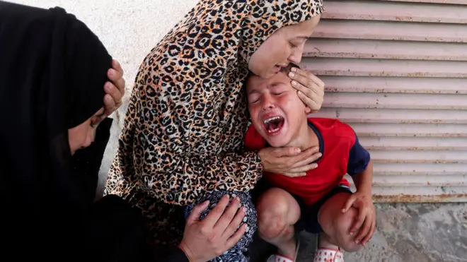 A young child cries while being comforted by a woman. 