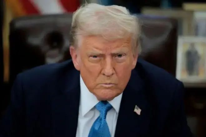 Presidente americano Donald Trump sentado e olhando firmemente para a câmera