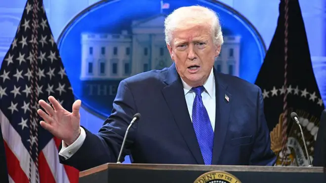 Trump kürsüde amerikan bayrakları önünde mikrofona konuşuyor