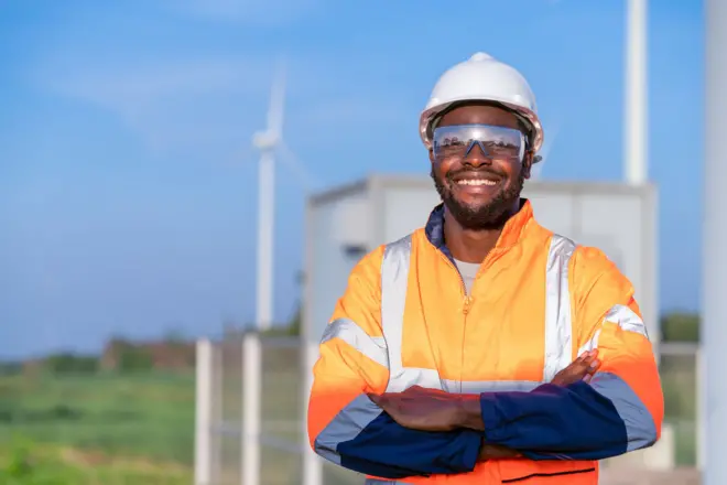 Un homme en tenue d'ingénieur pose devant des éoliennes