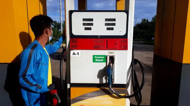 ဆီထည့်စက်တစ်ခုမှာ ဆီရောင်းနေတဲ့ အပြာရောင်လက်ရှည််အင်္ကျီဝတ်အမျိုးသားတစ်ဦး