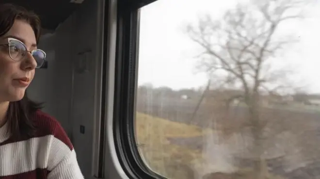 دختری که عینک به چشم دارد از کلکین قطار به بیرون نگاه می‌کند.