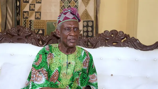 Bíṣọ́ọ̀bù Ladigbolu wọ aṣọ aláwọ̀ ewé tó sì jòkòó lórí àga