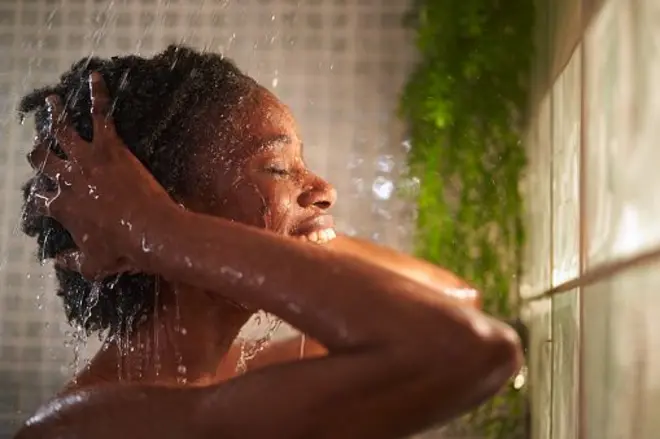 Jeune femme africaine prend une douche, se lavant les cheveux. 