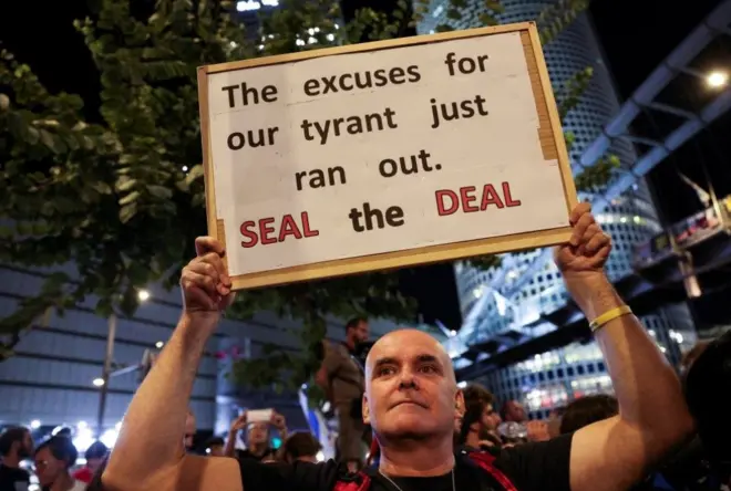 متظاهر إسرائيلي في تل أبيب يحمل لافتة، بينما يحتج الناس ضد الحكومة، للمطالبة باتفاق وقف إطلاق النار والإفراج الفوري عن الرهائن المختطفين إثر هجوم حماس في 7 أكتوبر/تشرين الأول 2023، كتب على اللافتة "انتهت أعذار طاغيتنا. أبرم الصفقة".