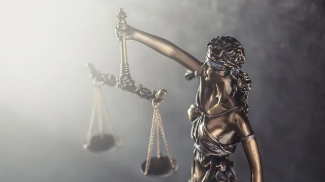 Statue symbolizing blindess of justice holds scales against the shining light.