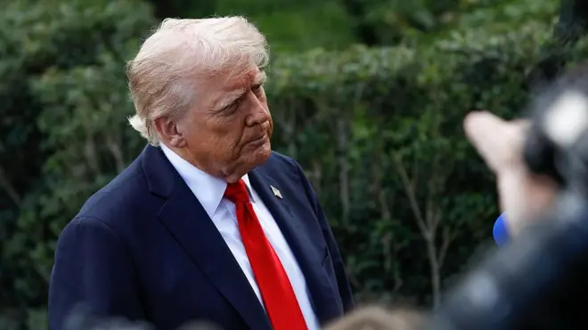 Дональд Трамп у синьому піджаку, білій сорочці та червоній краватці стоїть перед журналістами