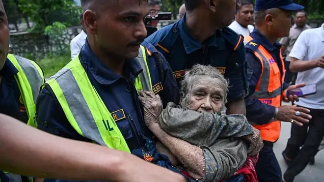 Rescatistas cargan a una anciana cubierta de barro en Nepal.