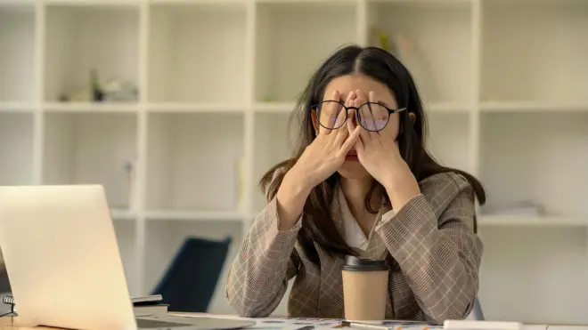 Жінка сидить перед комп'ютером і втомлено тре очі