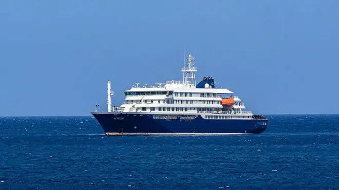 El crucero MV Hondius anclado frente al puerto de Praia, la capital de Cabo Verde, el 3 de mayo de 2026. Es una embarcación de gran tamaño, de color azul y blanco. 