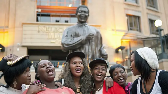 Some women pose in front of di famous Nelson Mandela statue for Sandton, Johannesburg