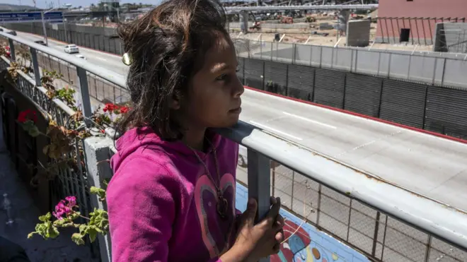 A young migrant girl looks on to the US border