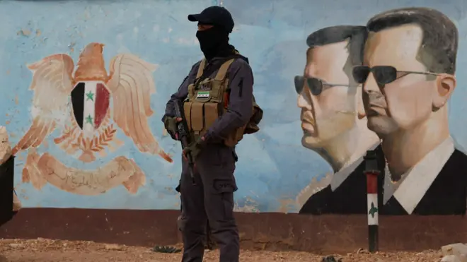 Сирийский сотрудник служб безопасности на фоне портретов Башара Асада, январь 2025, Дамаск