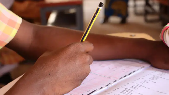 Student holding pencil shading exam paper