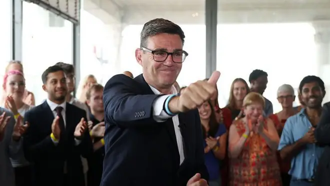 Andy Burnham İşçi Partisi lideri ilan edildikten sonra, baş parmağını olumlama amaçlı kaldırmış halde ve arkasında alkışlayan partililerle poz veriyor