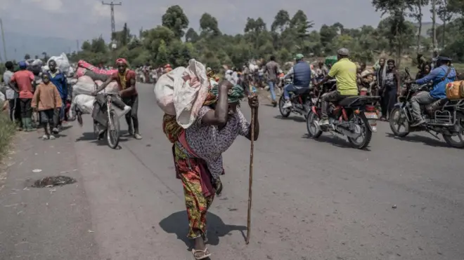 Umugore wikoreye bimwe mu byo atunze, mu gihe abantu bari barimo guhunga bava muri teritwari ya Masisi, mu ntara ya Kivu ya Ruguru, nyuma y'imirwano ikaze hagati y'inyeshyamba za M23 n'ingabo za Repubulika ya Demokarasi ya Congo, aha ni mu muhanda uri hafi y'i Sake, ku itariki ya 7 Gashyantare (2) mu mwaka wa 2024. 