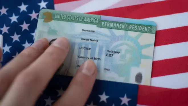 Una mano con una green card y una bandera de EE.UU. abajo
