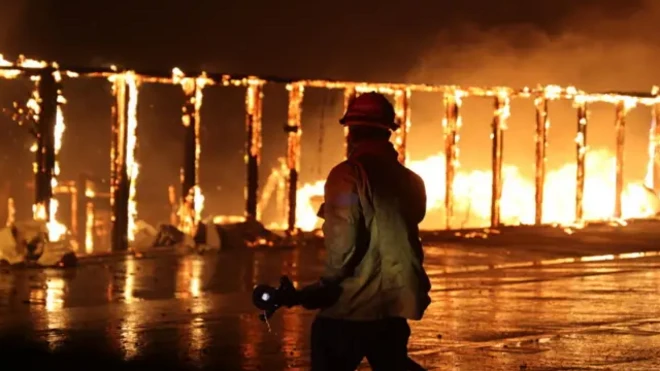 Firefighter battling the LA fires with a burning structure in the background