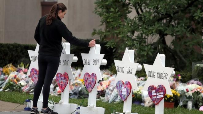 在匹兹堡的“生命之树”犹太教堂外，一名妇女站在哀悼枪击事件遇害者的鲜花和悼念物品前。