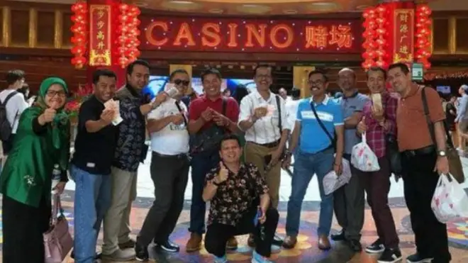 Pose santai dengan acungan uang di depan kasino.