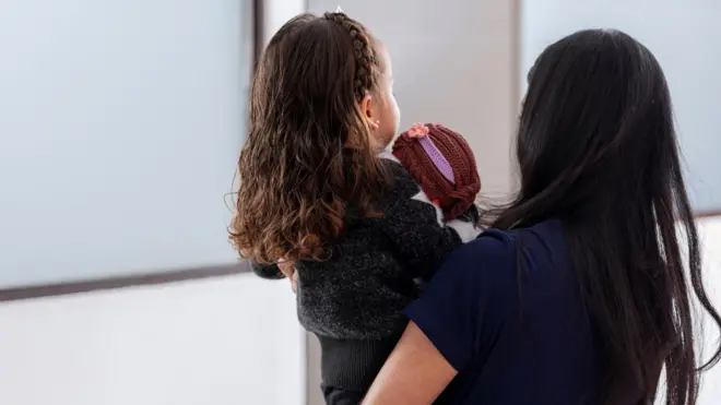vistas de costas, mulher com cabelo preto e criança com cabelo castanho em seu colo 