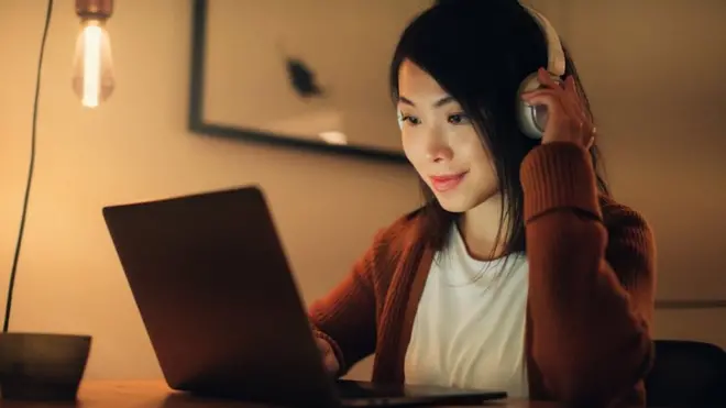 A woman listening to headphones while sat at a laptop