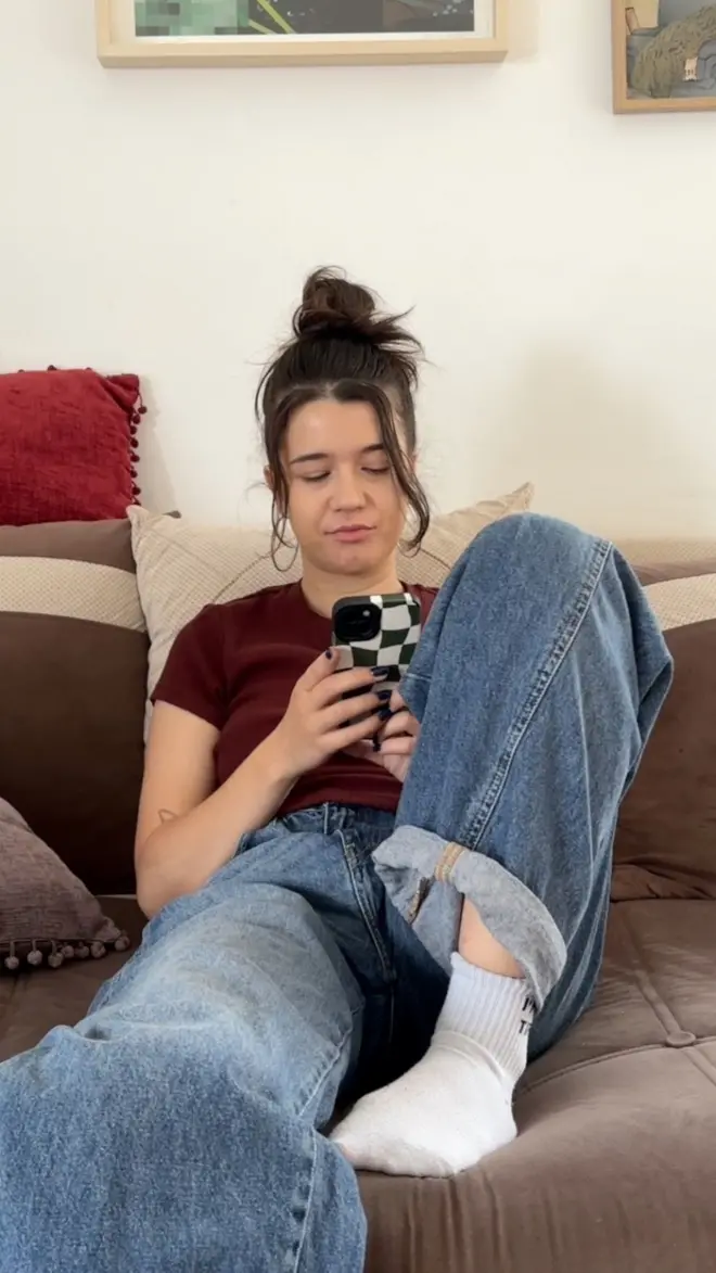 Reporterka sedi na kauču i gleda u telefon.