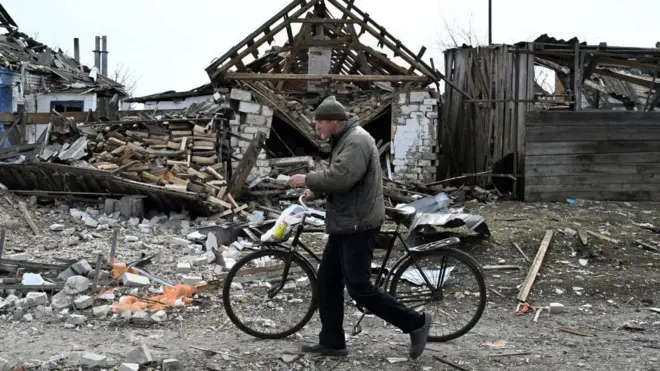 Чоловік із велосипедом іде повз зруйновані будівлі на прикордонні Сумщини