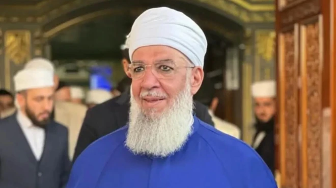 Cemaatin önde gelen isimlerinden Muhammed Saki Erol'un fotoğrafı. Erol'un üzerinde mavi bir elbise bulunuyor. 